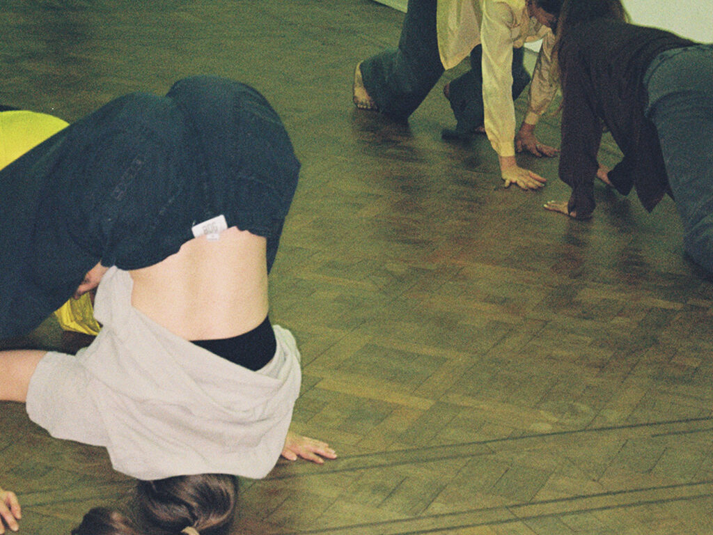 Performers improvising movements on the floor in an empty room with white walls.