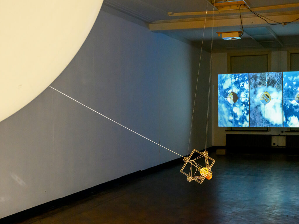 Image of a view of the exhibition depicting a part of an installation and visual media depicting pudding and satellite view.
