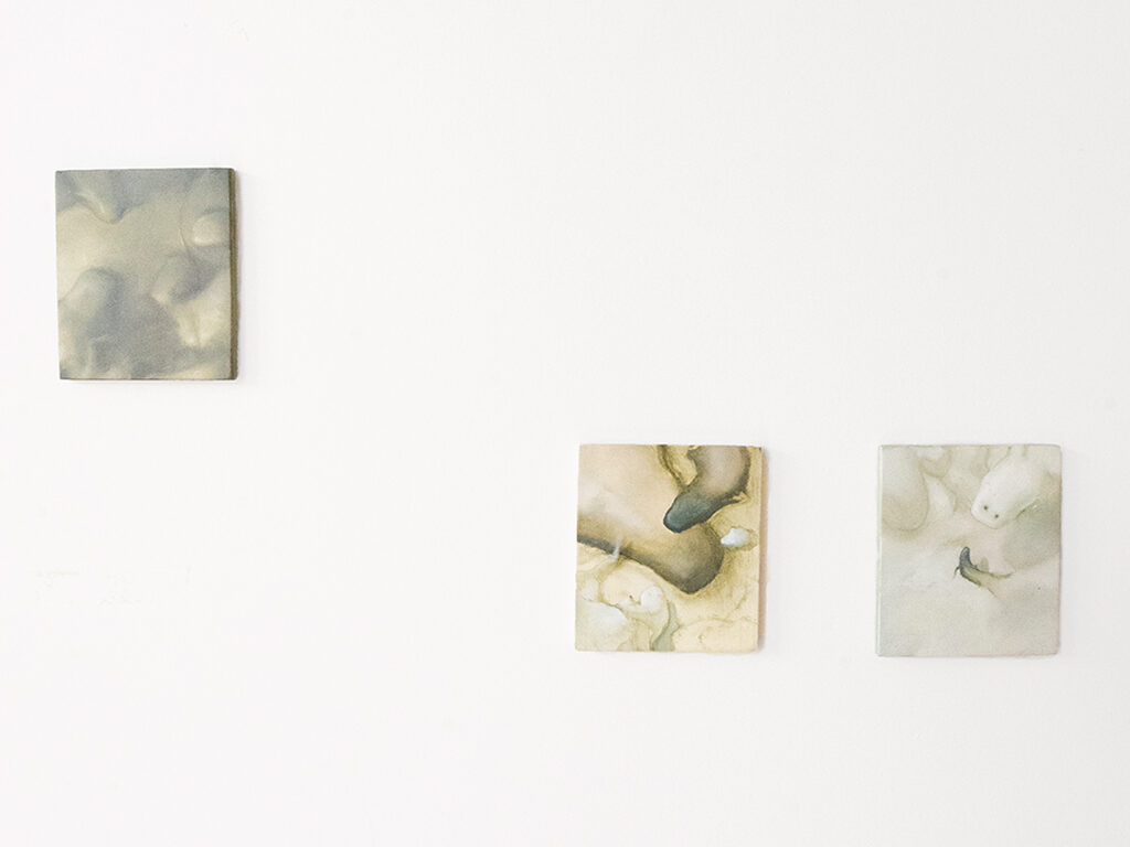 Three small compositions made with oil paint hanging on a white wall.