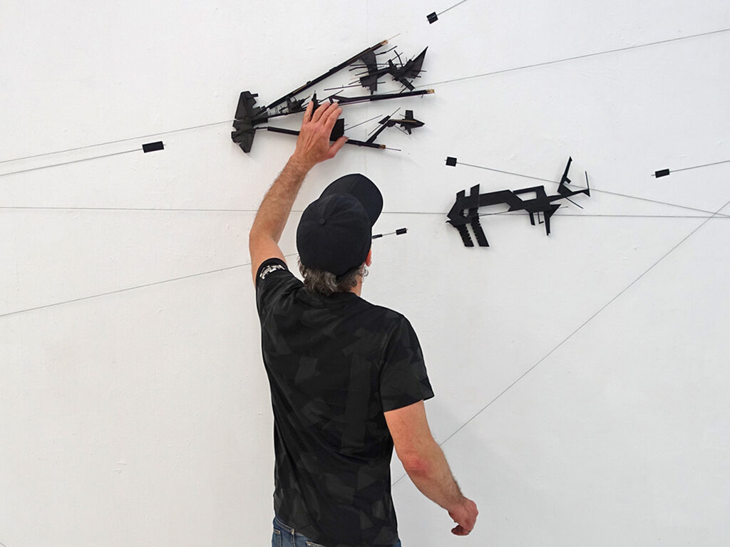 Composition on a white wall. In front the artist interacting with it.