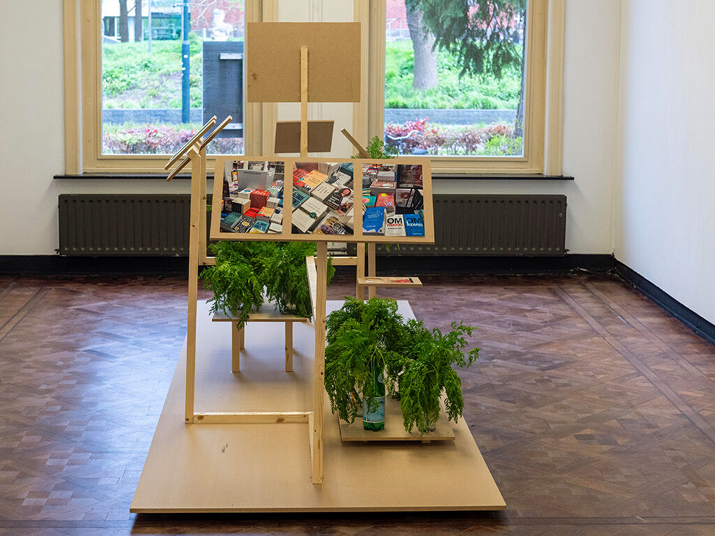 A wooden structure in the middle of a room. On top the structure there are some plants and images.