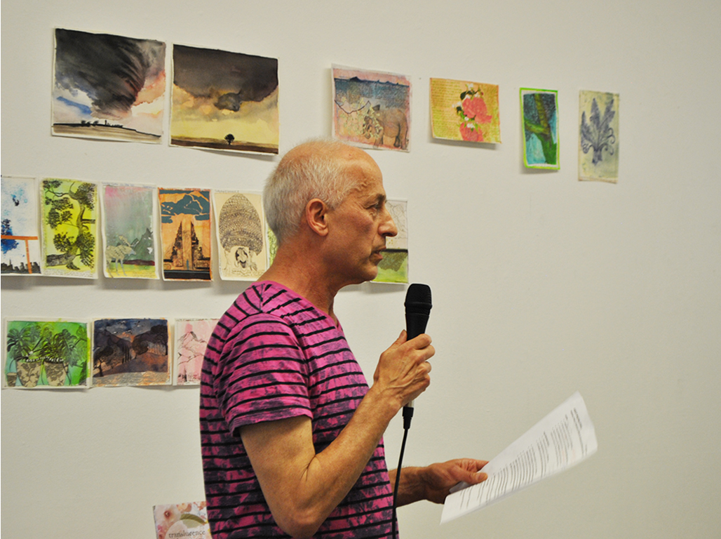 A speaker giving a lecture. Behind some paintings hanging on the wall.
