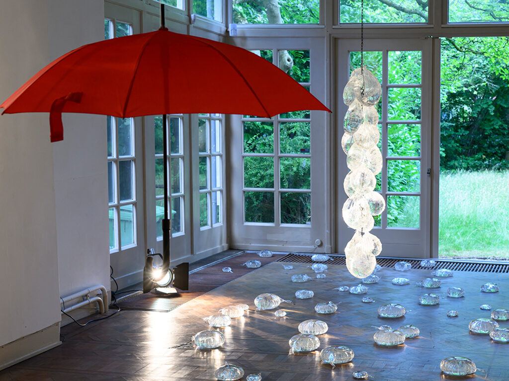 Installation consisting in a red umbrella hanging from the ceiling and transparent shapes scattered around the room.
