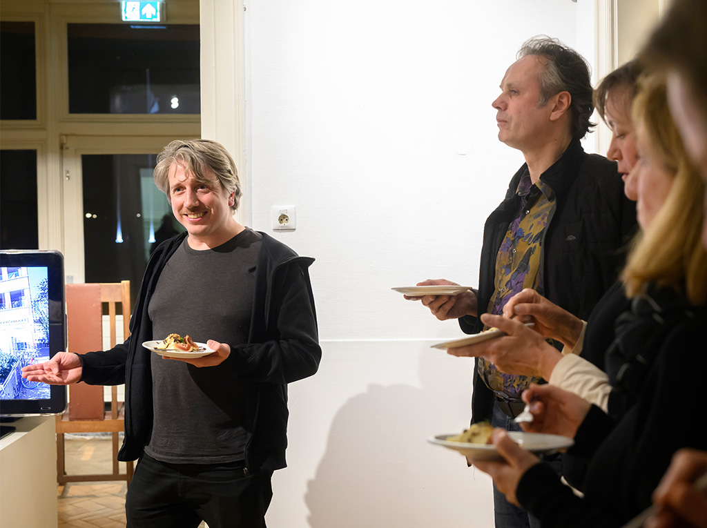 People standing while enjoying some food and listening to a presentation.