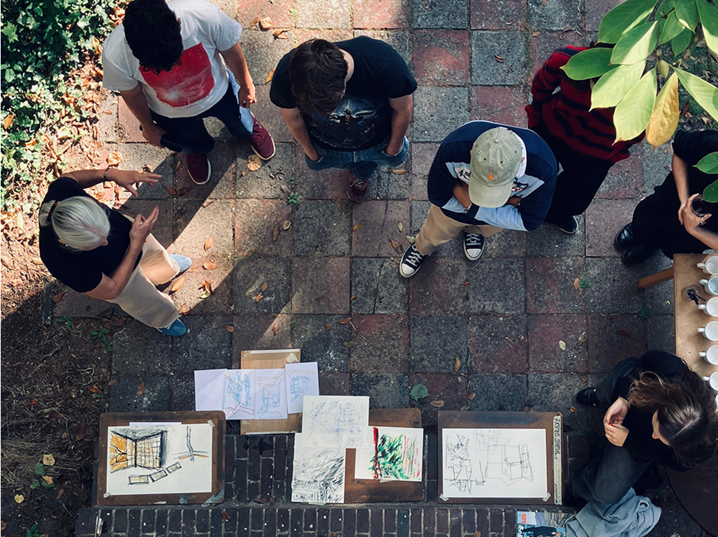 Top view of sketches scattered on a surface and students observing them.
