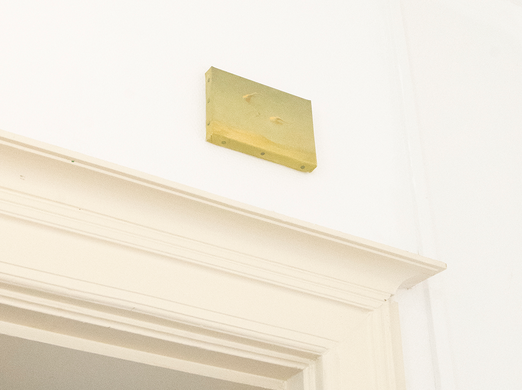 Small yellowish oil paint hanged on the wall on top of a door frame.