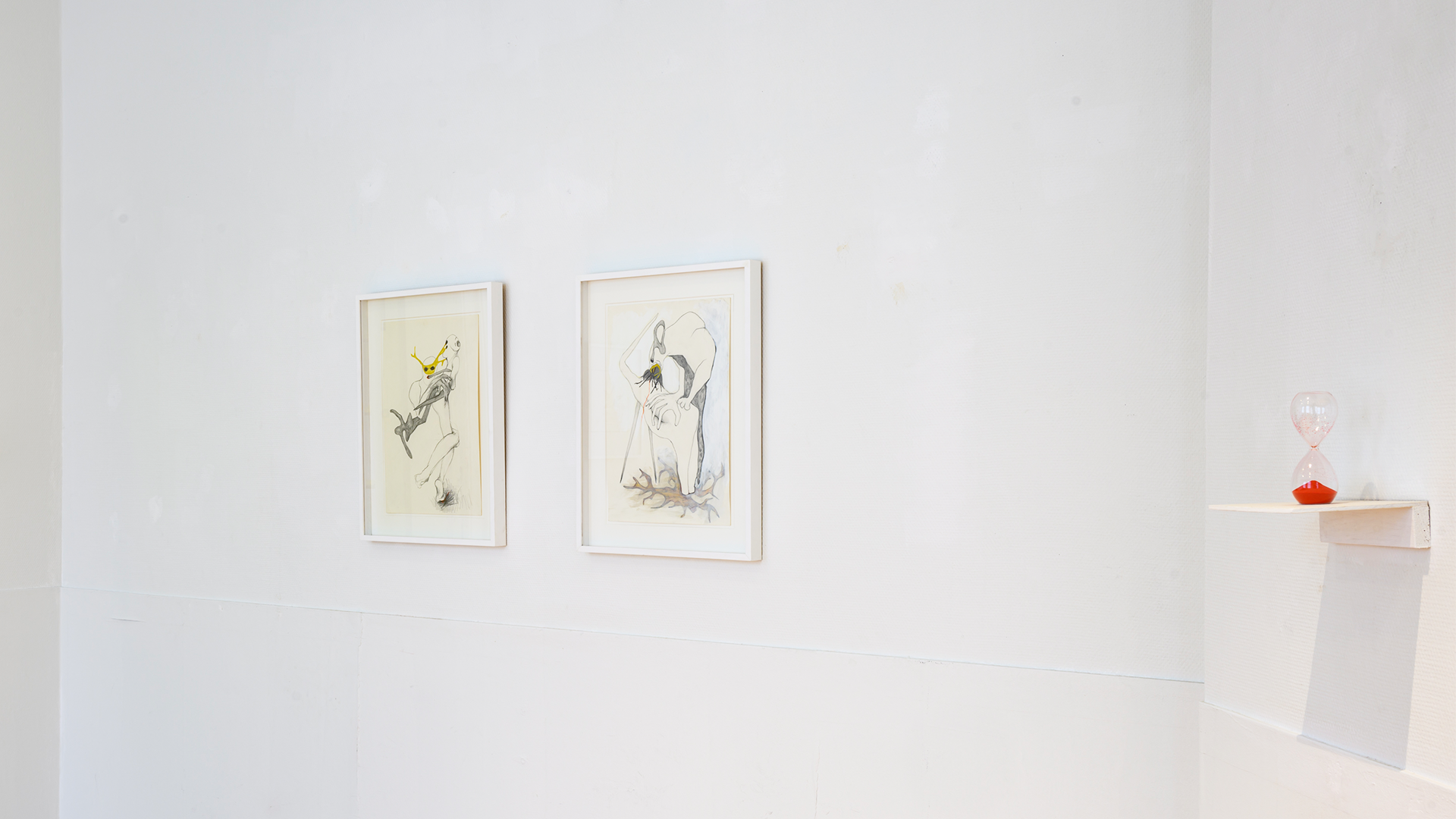 Two frames and a red sand clock hanging from a white wall