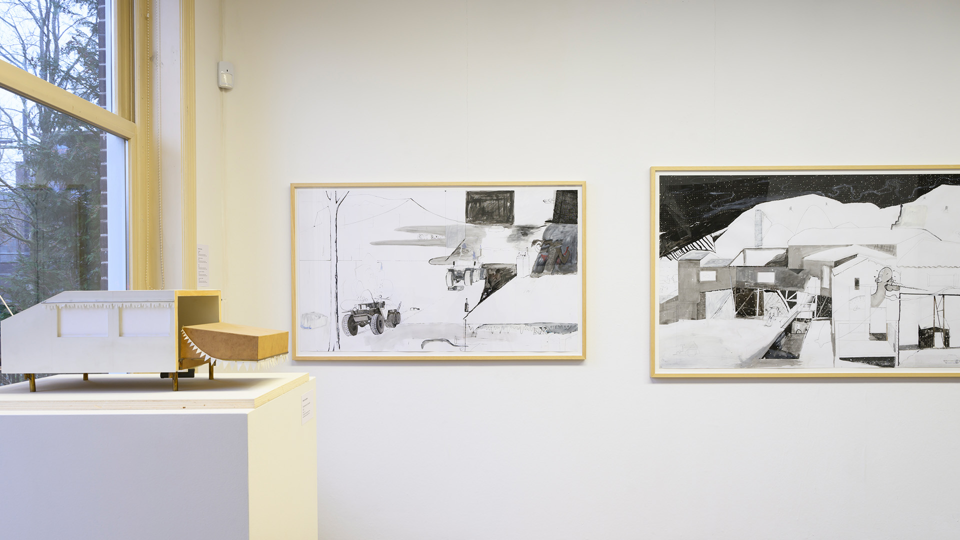 Art frames framed and hang on a white wall next to a podium with a maquette.