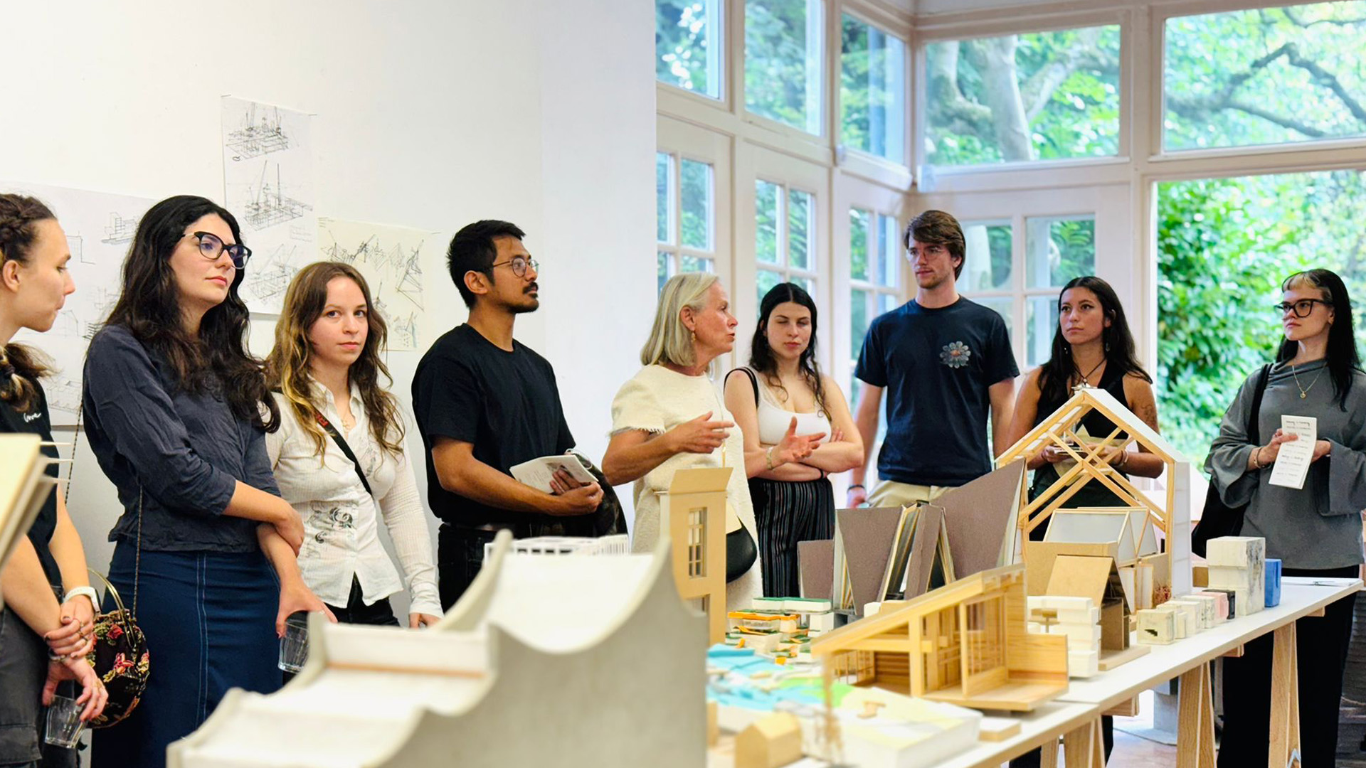 Architecture maquette displayed on a table while group of students gathered around listening to a presentation.
