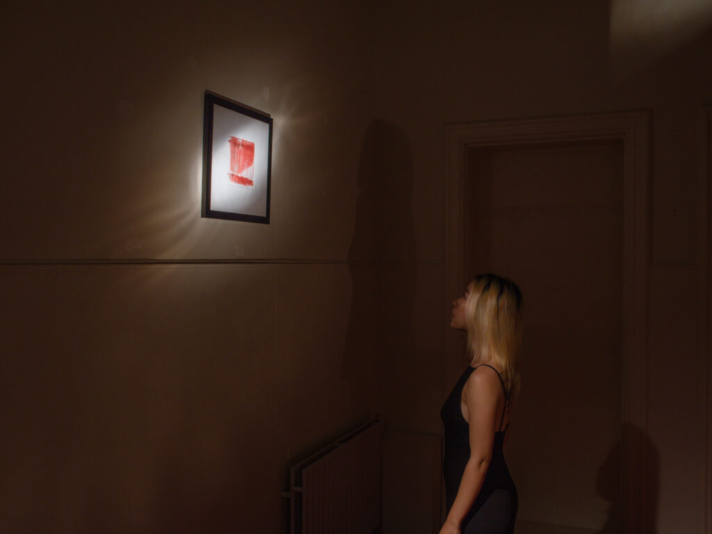 Woman with blonde hair and a black dress standing in front of a light screen