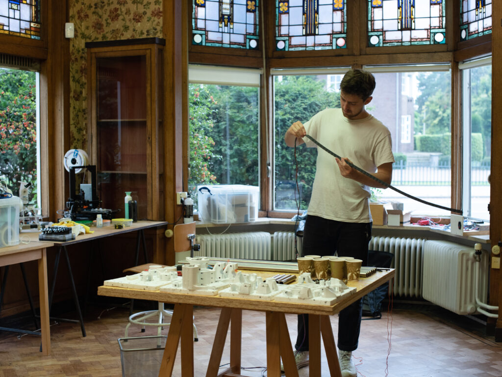 Person standing in front of a table, in a room with stained glass and old school walpaper