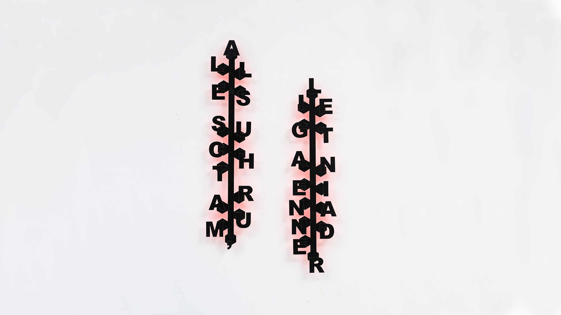 Two vertical, black typographic wall sculptures mounted on a white wall. Each piece has a central spine that connects the letters.