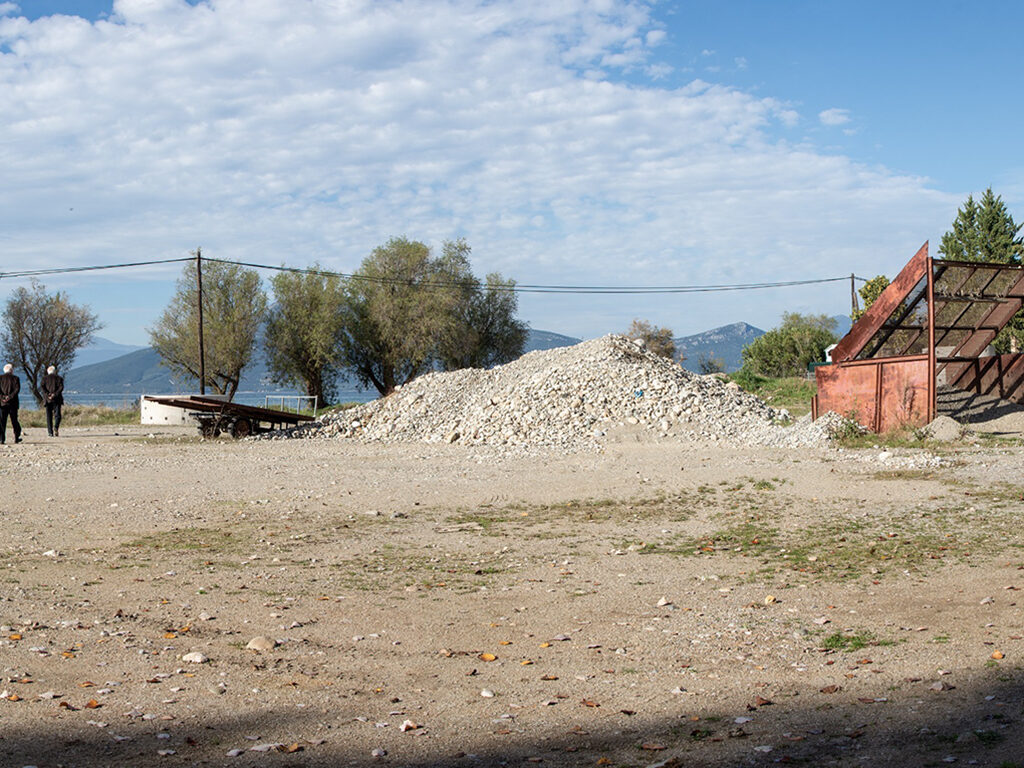 Landscape picture consisting of a red half done house and two man walking around