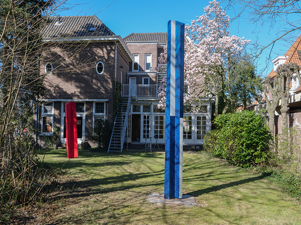 A picture of a house garden with a blue art piece standing in the middle.