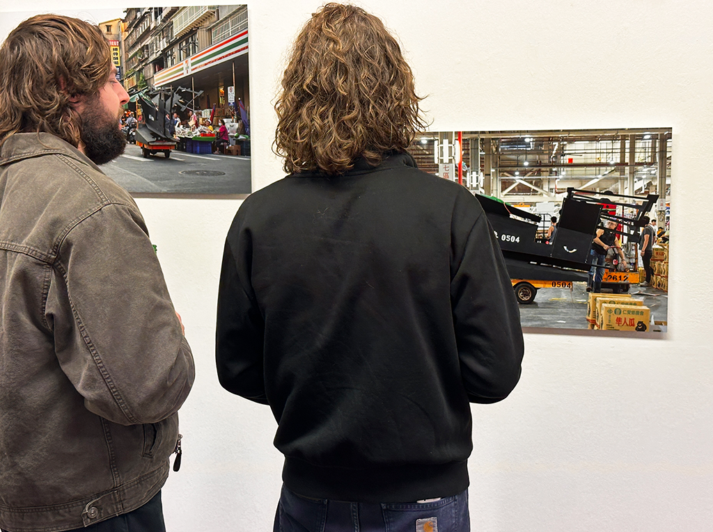 Visitors watching carefully two images frames hanging on a white wall.