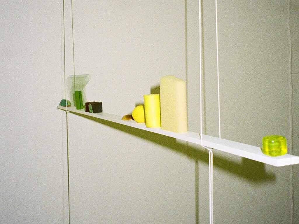 A shelf hanging from the ceiling with two ropes, showcasing an arrangement of small yellow and green objects.