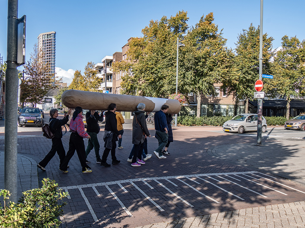 A group of persons walking around the city carrying a big cigar together.