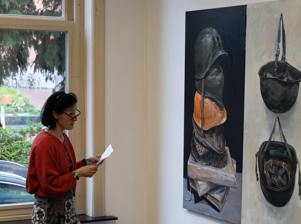 A big painting hanging from the wall, and a woman with a paper analyzing the painting.