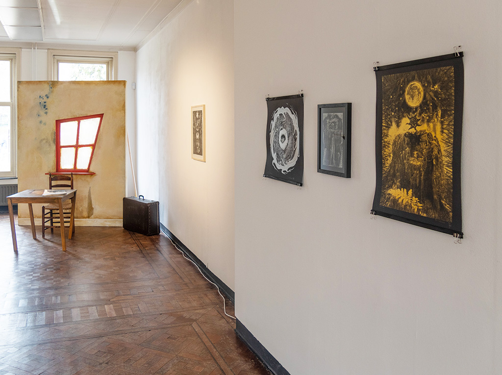 Image of the exhibition view facing the window with an installation in front of it and four artworks on the right wall.