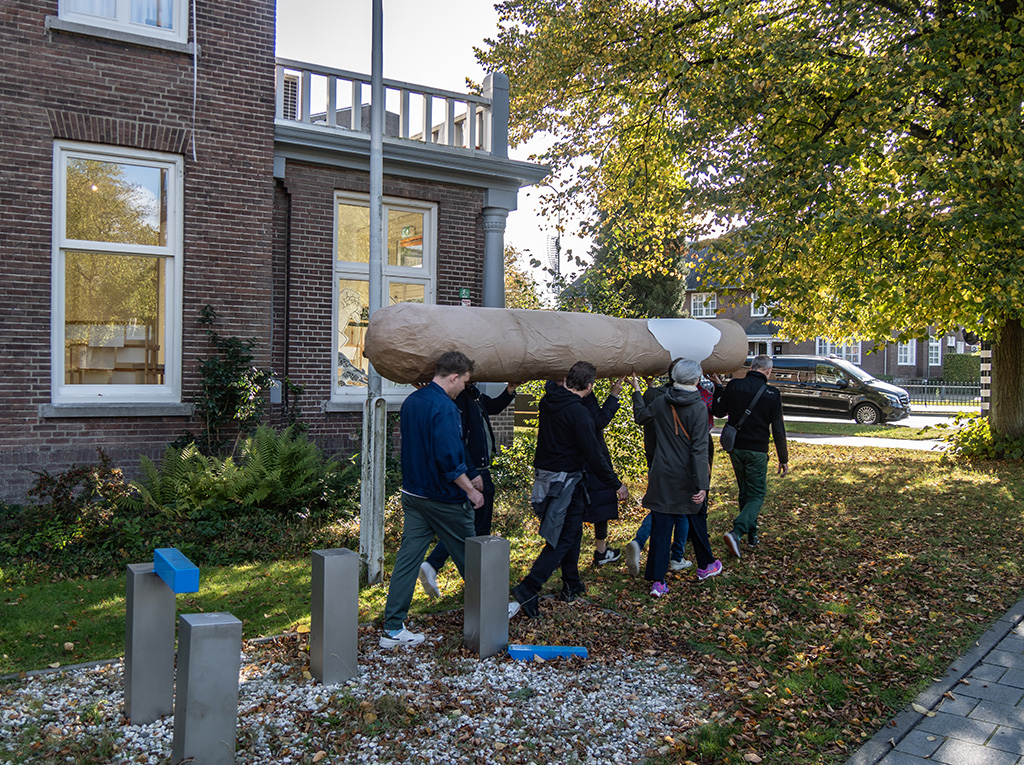 A group of persons walking around the city carrying a big cigar together.