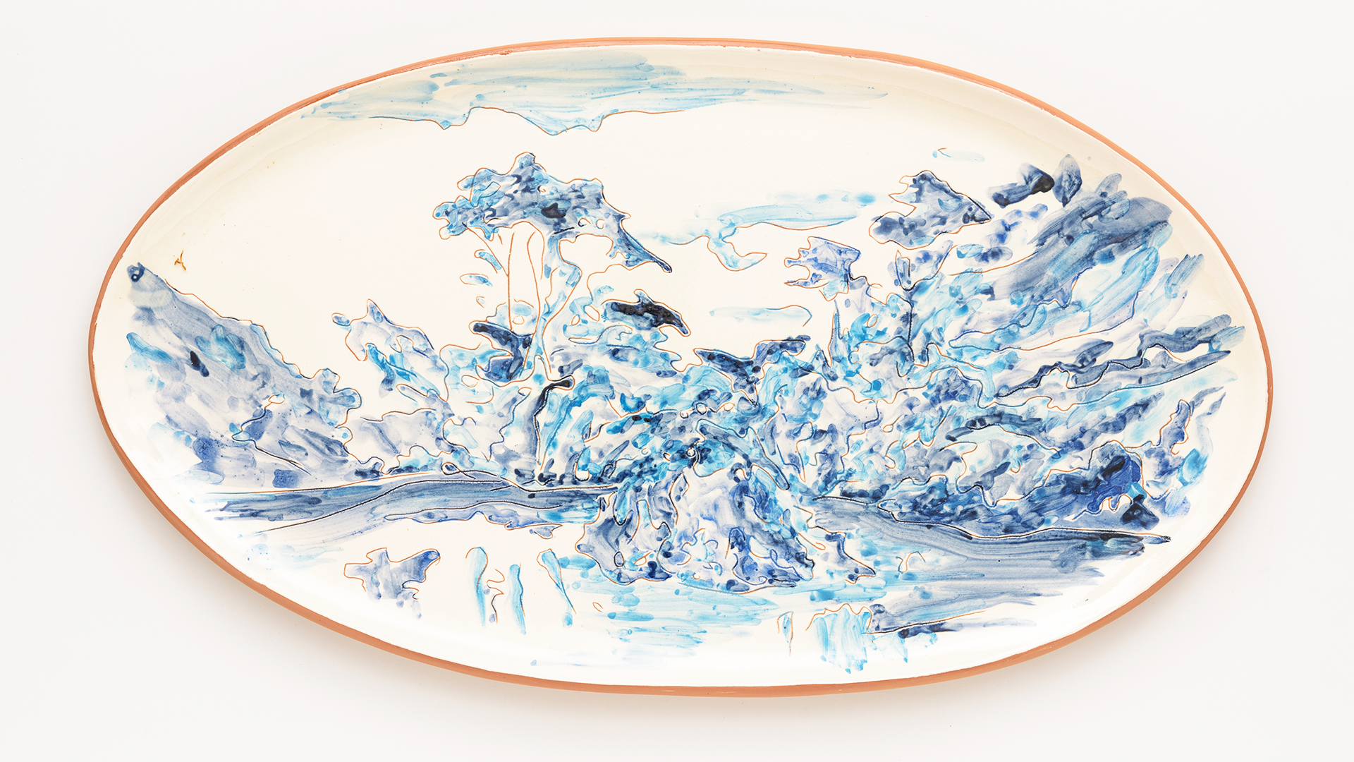 Image if an oval ceramic platter with a terracotta rim, decorated with an abstract blue landscape resembling splashing water or rocky terrain.