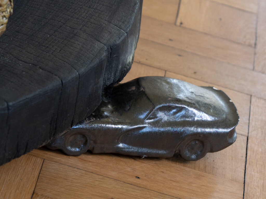 A small sculpture of a car crashing onto a large, round black form.