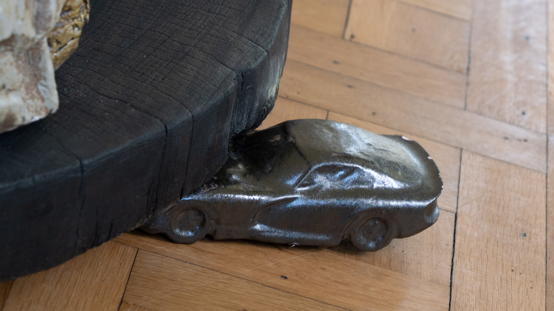 A small sculpture of a car crashing onto a large, round black form.