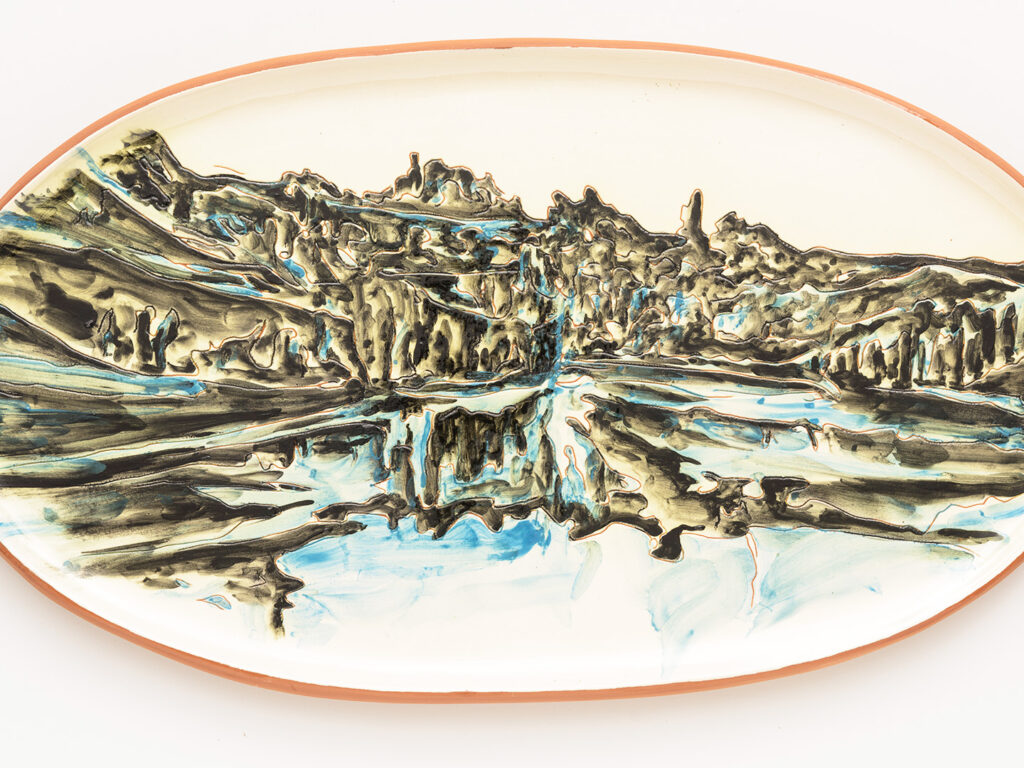 Image of an oval ceramic platter with a terracotta rim, decorated with an abstract green-blue landscape resembling a mountains, forests and waterfalls.