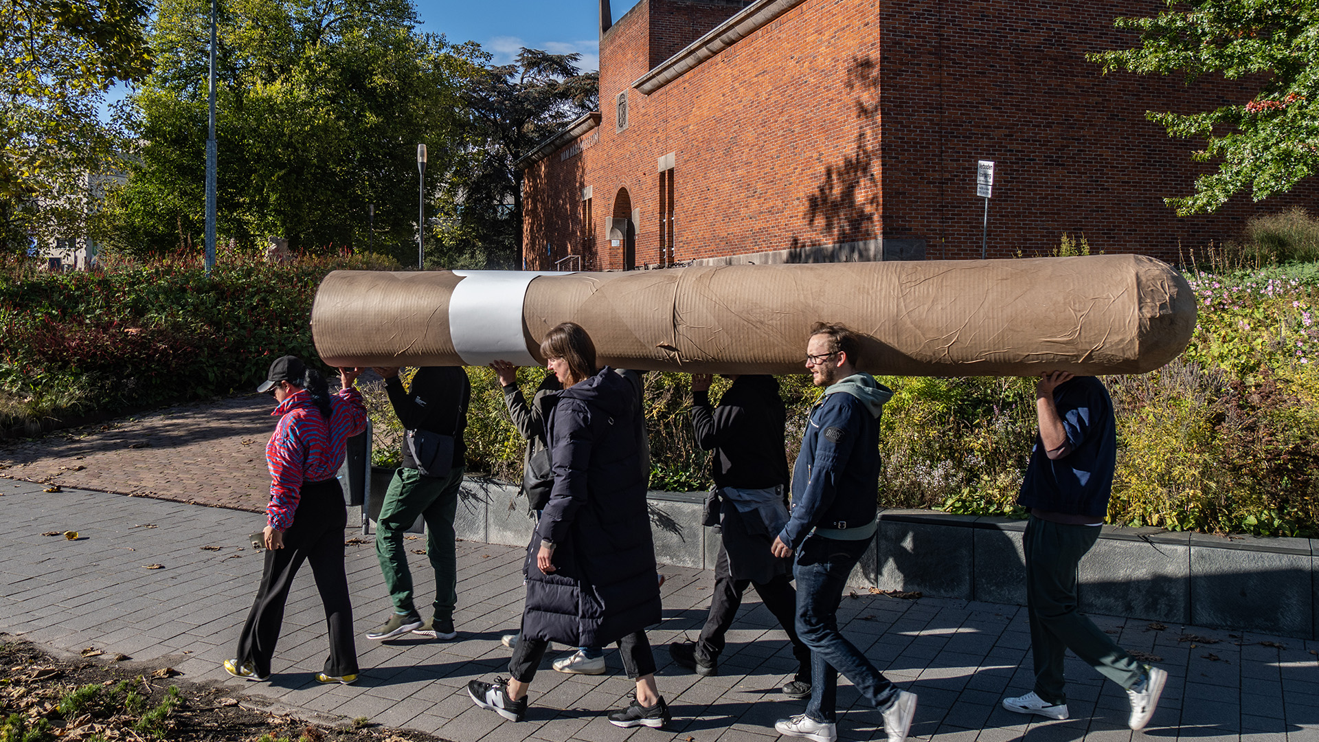 A group of persons walking around the city carrying a big cigar together.